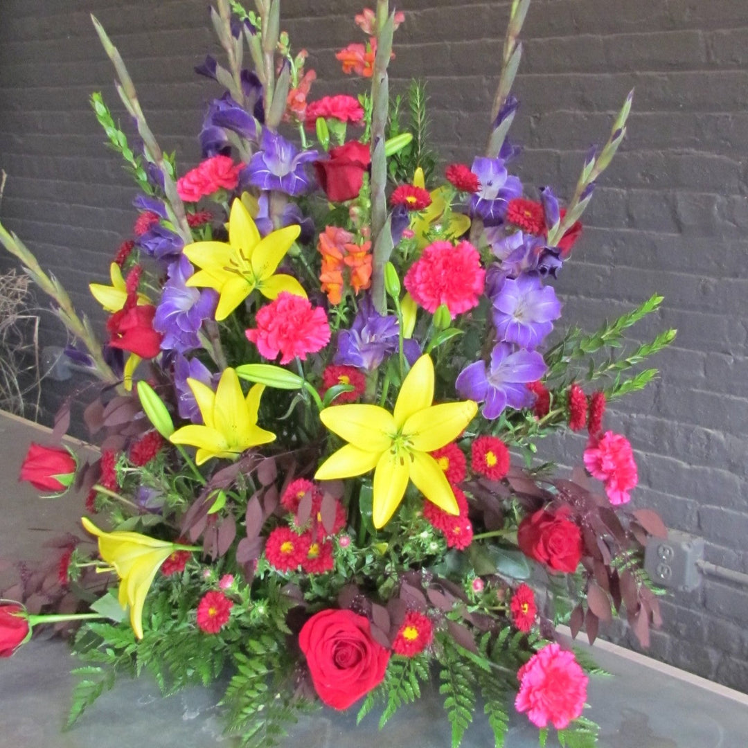 Large multi-colored funeral arrangment with purple, yellow, and red flowers
