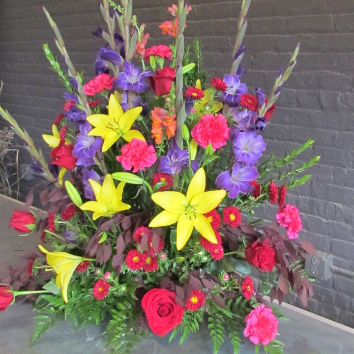 Large multi-colored funeral arrangment with purple, yellow, and red flowers